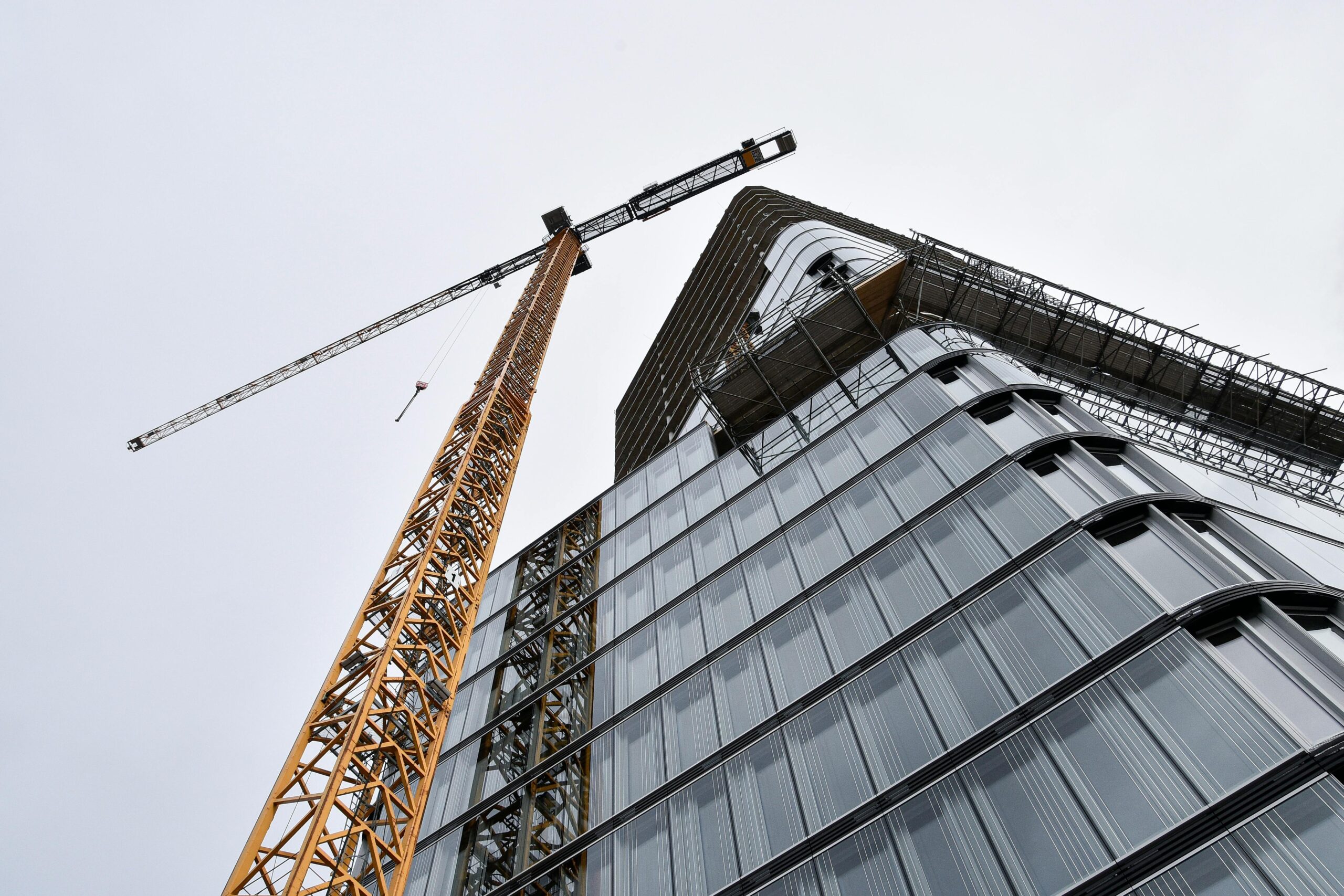 A low angle shot of modern building under construction with a crane viewed against the sky.
